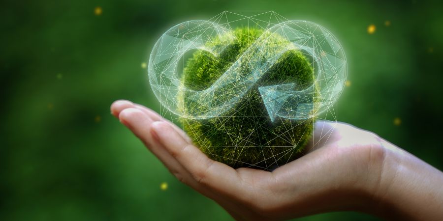 Auf dem Bild ist eine Hand zu sehen, in der ein rundes Grasbüschel liegt. Im Vordergrund ist ein transparenter Pfeil in Form eines Unendlichkeitszeichen abgebildet.