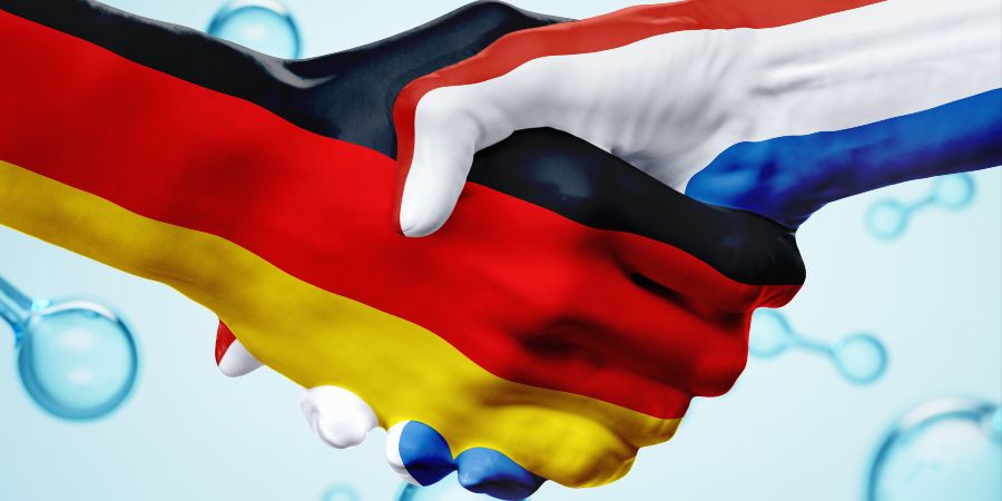 Das Bild zeigt einen Handschlag. Eine Hand hat die Farben der Deutschland-Flagge, die andere Hand die Farben der Niederlande-Flagge. Im Hintergrund sind Wasserstoff-Blasen zu sehen.