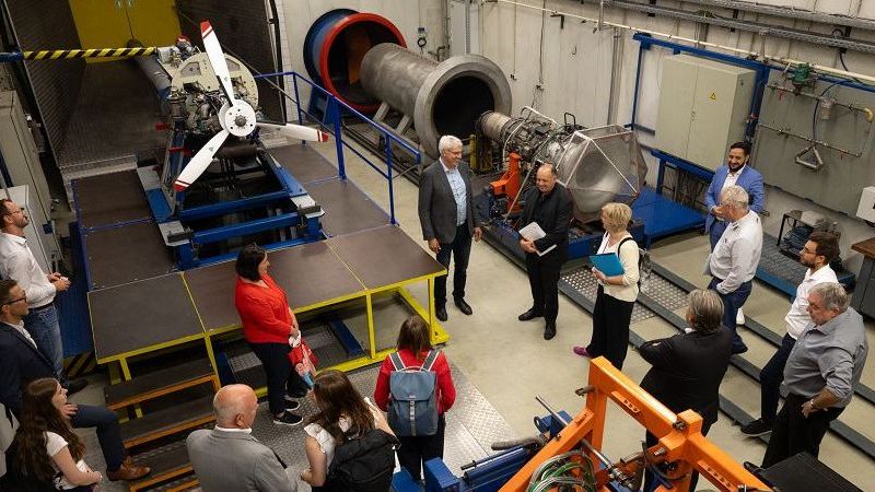 Das Bild zeigt viele Menschen, die auf einen Propeller schauen.