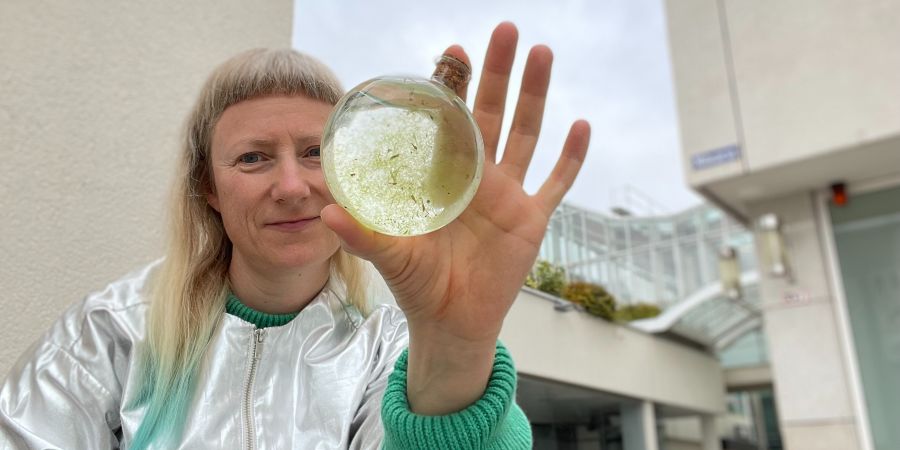 Das Bild zeigt Line Krom auf einer Ausstellung im Nordwestzentrum in Frankfurt. Sie hält ein Glasgefäß in der Hand, in dem sich Algen im Wasser befinden.