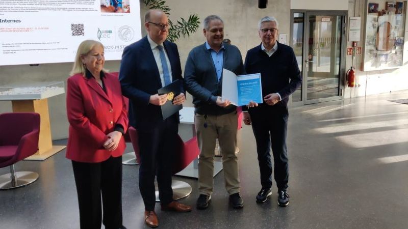 © PtJ Das Bild zeigt unter anderem Staatssekretär Hauer und Prof Sigfried Waldvogel (Sprecher des Zukunftsclusters ETOS). Waldvogel hält die Förderurkunde in der Hand.