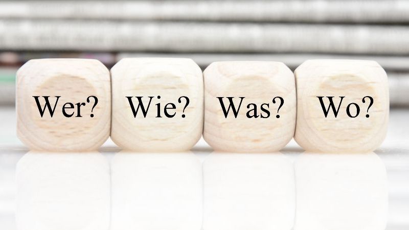 Das Bild zeigt vier Würfel auf denen die Wörter Was? Wer? Wo? Wann? geschrieben stehen.