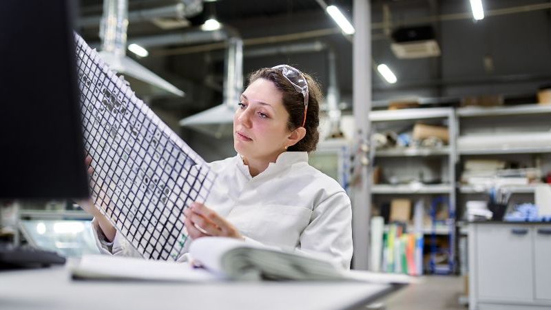 Das Bild zeigt eine Forscherin, die eine Materialprobe begutachtet.