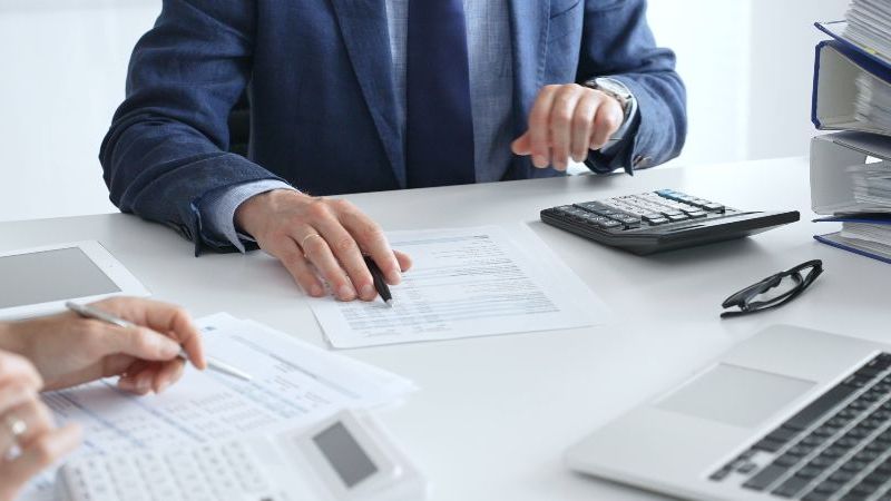 © rogerphoto – stock.adobe.com Das Bild zeigt einen Schreibtisch mit Unterlagen und Händen von arbeitenden Menschen.