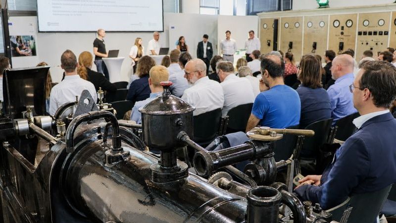 © PtJ Dieses Bild zeigt Teilnehmende eines Seminars in einem historischen Maschinenraum, die einer Präsentation vor einer großen Industrieanlage folgen.