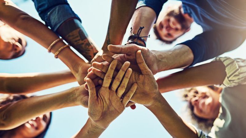 © peopleimages.com – stock.adobe.com Das Bild zeigt Menschen, die ihre Hände übereinander legen.