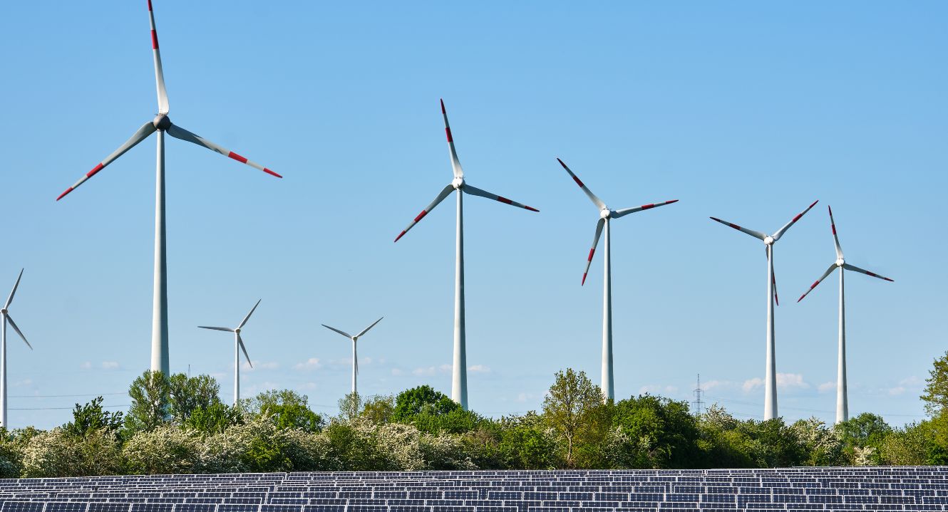 Im Vordergrund ist eine Photovoltaikanlage zu sehen, im Hintergrund mehrere Windkraftanlagen.