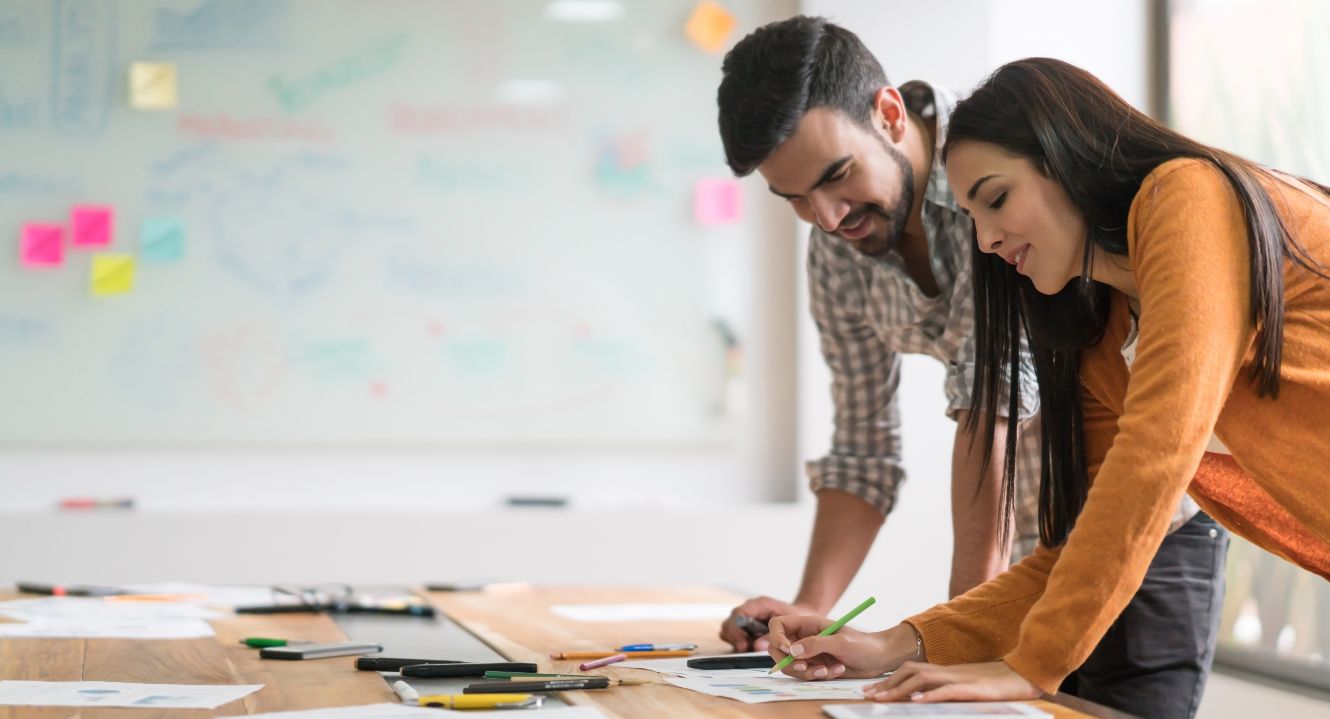 Auf dem Bild sieht man mehrere Männer und Frauen, die an einem Tisch zusammen sitzen und mit einander sprechen. Die Umgebung sieht modern aus.