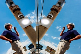 The image shows a man with a helmet in front of a solar tower.