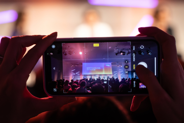 Das Bild zeigt ein Smartphone, welches Menschen auf der Bühne bei der Auftaktveranstaltung des Wissenschaftsjahres 2025 fotografiert. 
