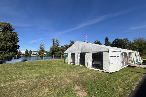 Unser großes weißes Veranstaltungszelt am Ufer des FZJ-Teichs, bei sonnigem Himmel auf einer grünen Wiese. 