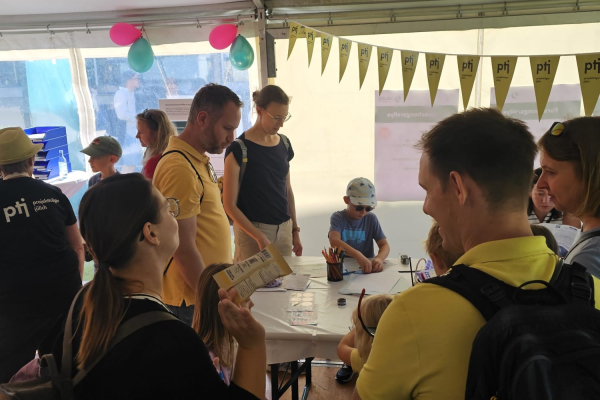 Mehrere Erwachsene und Kinder in einem Aktionszelt versammeln sich um einen Basteltisch mit Stiften und Papier. 